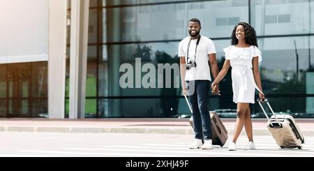 Couple heureux marchant avec des bagages à l'extérieur du bâtiment de l'aéroport Banque D'Images