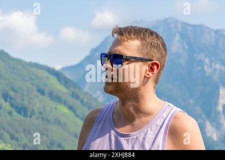 Un homme de 40-45 ans portant des lunettes de soleil. Il est debout devant un lac avec des montagnes en arrière-plan. Banque D'Images