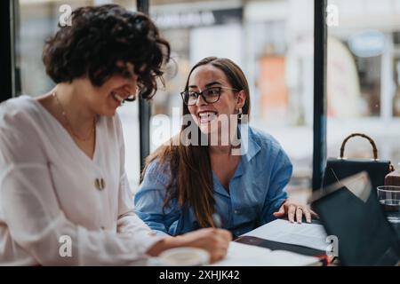 Deux femmes d'affaires collaborant joyeusement ensemble dans une configuration de café moderne Banque D'Images