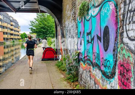 Une dame court le long d'un sentier le long du bras de Paddington du Grand Union canal devant une tente appartenant à un sans-abri à Londres, au Royaume-Uni Banque D'Images