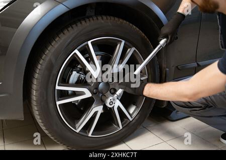 Mécanicien serrage des écrous de roue avec clé dans l'atelier de réparation automobile Banque D'Images