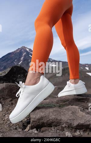 Jambes féminines athlétiques portant des leggings coupe orange et des baskets blanches. Gros plan de la partie inférieure du corps musculaire de la femme pendant l'entraînement de fitness en plein air dans Banque D'Images