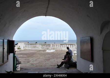 Vue du golfe de Guinée depuis une cour intérieure, Cape Coast Castle, Cape Coast, Ghana - personnes assises à l'entrée, Banque D'Images