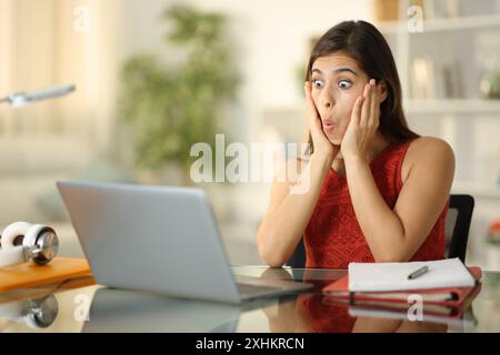 Étudiant étonné de vérifier le contenu de son ordinateur portable assis à la maison Banque D'Images