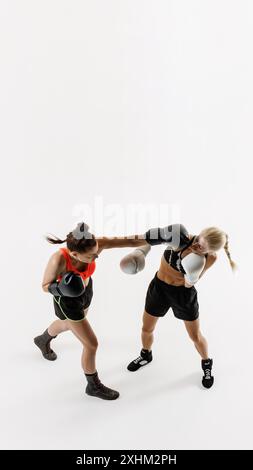 Image verticale vue de dessus de deux femmes compétitives, athlètes de boxe rivalisant farouchement dans un match de boxe isolé sur fond blanc Banque D'Images