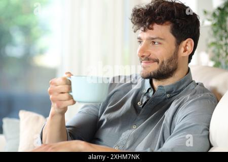 Homme heureux buvant du café assis dans un intérieur de maison regardant loin Banque D'Images