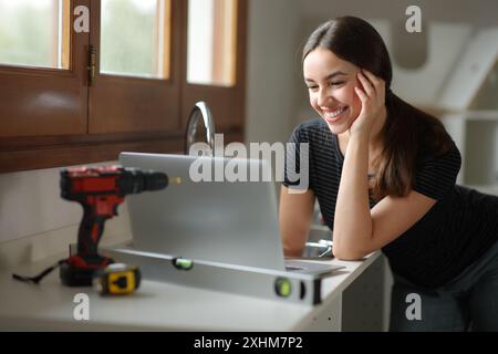 Femme heureuse planifiant la rénovation de la maison en ligne avec un ordinateur portable Banque D'Images