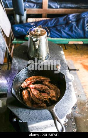 Bacon frit dans une poêle en fonte sur un poêle à bois au camp Banque D'Images