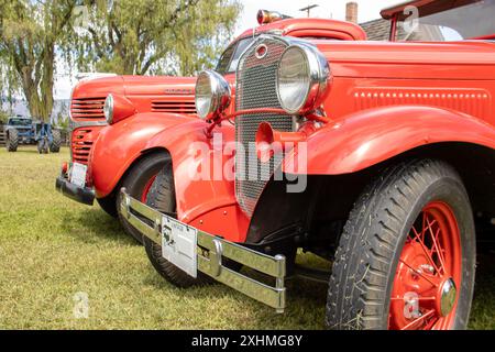 Voitures rouges vintage exposées à l'extérieur, avec des tracteurs en arrière-plan Banque D'Images