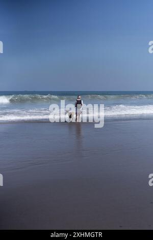 Une femme marche le long de la plage avec son chien Golden retriever. Banque D'Images