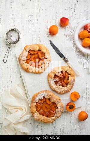 Galette d'abricot. Fait maison trois petites tarte à l'abricot avec l'abricot frais servi pour la partie de thé d'été sur fond de table lumineuse en bois vieux. Fam. Traditionnel Banque D'Images