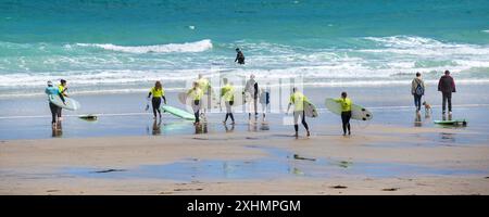 Une image panoramique d'un instructeur de surf de l'Escape Surf School et d'un groupe de débutants de surf marchant dans la mer pour une leçon de surf sur la plage de Towan Banque D'Images