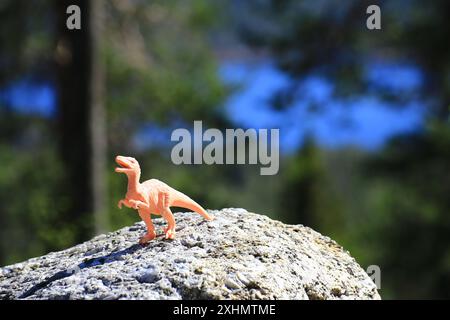 Dinosaure jouet en plastique équilibré au sommet d'un grand rocher dans le parc national de Bjornlandets, Suède. Banque D'Images