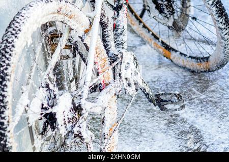 Vélo est recouvert de mousse blanche. Bicyclette de lavage avec jet de mousse au lavage de voiture. Libre-service. Gros plan Banque D'Images