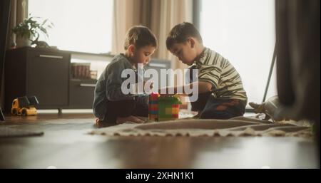 Portrait de deux enfants asiatiques masculins jouant avec des blocs de construction colorés dans leur chambre pendant la journée. Grand frère aidant le jeune frère à construire une maison de jouet. Concept d'enfance et d'innocence Banque D'Images