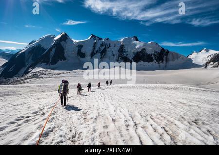 Groupe d'alpinistes avec sacs à dos est enfilé ensemble et ascendant sur Glacier dans les montagnes enneigées Banque D'Images