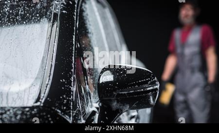 Studio cinématique gros plan avec un SUV familial électrique respectueux de l'environnement debout dans une voiture Wash. Le véhicule est recouvert de mousse et doit être nettoyé dans un atelier d'entretien avant d'être vendu à un propriétaire Banque D'Images