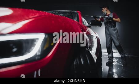 Expert en lavage de voiture utilisant une laveuse à pression d'eau pour nettoyer une voiture de sport moderne rouge. Homme adulte lavant la saleté, préparant une voiture de muscle américaine pour le détail. Vidéos cinématographiques créatives avec Luxury Vehicle Banque D'Images