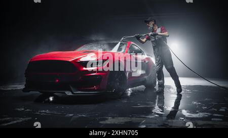 Expert en lavage de voiture utilisant une laveuse à pression d'eau pour nettoyer une voiture de sport moderne rouge. Homme adulte lavant la saleté, préparant une voiture de muscle américaine pour le détail. Photo cinématographique créative avec véhicule de luxe Banque D'Images