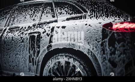 Studio cinématique gros plan avec un SUV familial électrique respectueux de l'environnement debout dans une voiture Wash. Le véhicule est recouvert de mousse et doit être nettoyé dans un atelier d'entretien avant d'être vendu à un propriétaire Banque D'Images