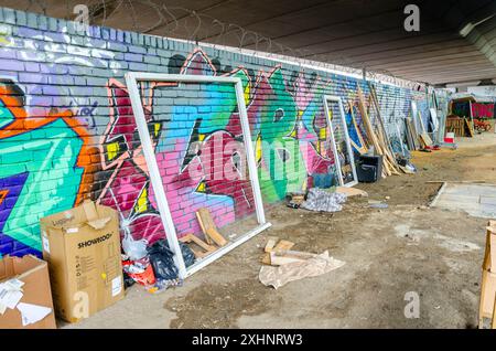 Déchets et morceaux de bois abandonnés contre un mur couvert de graffitis sous le pont de Westway le long du Grand Union canal à Londres, Royaume-Uni Banque D'Images