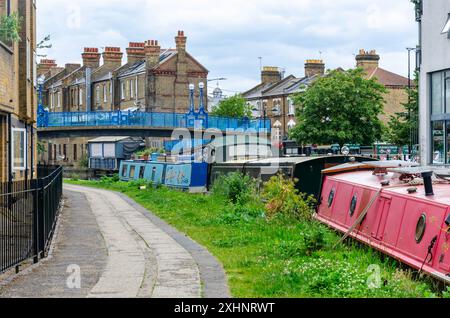 Une vue le long du Grand Union canal, Paddington Arm à Londres, Royaume-Uni avec des bateaux étroits amarrés et une passerelle traversant le canal Banque D'Images