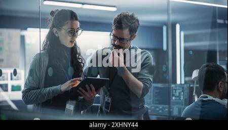 Portrait de deux jeunes ingénieurs créatifs, femmes et hommes, utilisant un ordinateur tablette pour analyser et discuter de la façon de procéder avec le logiciel d'intelligence artificielle. Debout dans High Tech Research Office Banque D'Images