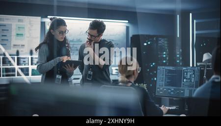 Portrait de deux jeunes ingénieurs créatifs, femmes et hommes, utilisant un ordinateur tablette pour analyser et discuter de la façon de procéder avec le logiciel d'intelligence artificielle. Debout dans High Tech Research Office Banque D'Images