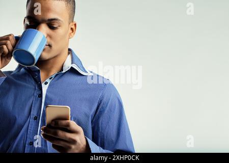 Individuel au look serein, tenant une tasse à café bleue et un smartphone. Vêtu d'une chemise bleue, il semble profiter d'un moment paisible et d'un séjour Banque D'Images