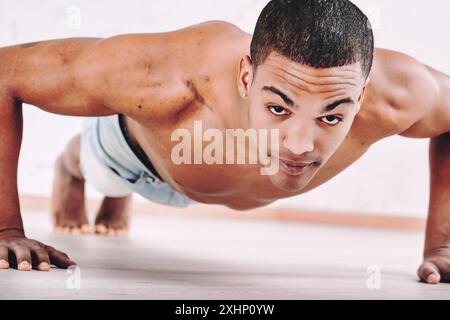 Jeune homme effectuant des pompes, présentant un physique solide et en forme. Son expression ciblée et ses cheveux courts soulignent son dévouement aux fitnes physiques Banque D'Images