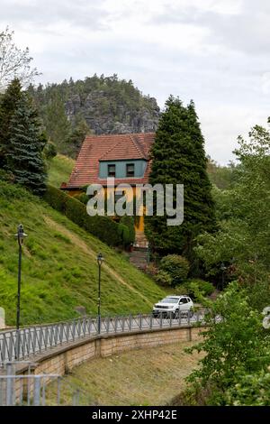 Une maison avec un toit vert se trouve sur une colline. Une voiture descend la route devant la maison Banque D'Images