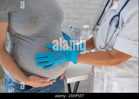 Femme enceinte consultant un médecin. Gynécologue caucasienne âgée tient les mains sur le ventre d'une patiente enceinte. Banque D'Images