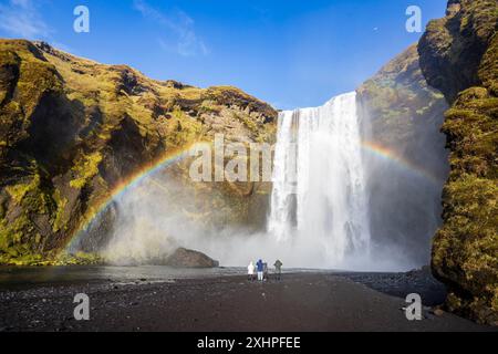 Islande, région de la Sudurland, Skógar, figures contemplent un arc-en-ciel devant les chutes de Skógafoss, 60 mètres de haut et 25 mètres de large Banque D'Images