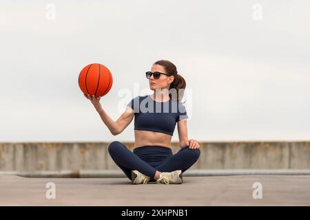 Fit femme sportive assise jambes croisées tenant un concept de basket-ball, de sport et de fitness. Banque D'Images