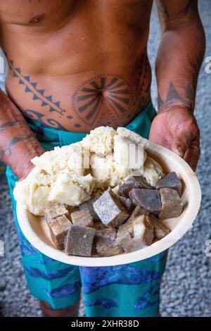 Polynésie française, île de Tahiti, Polynésienne tatouée tenant une assiette de morceaux de taro et de pain à la noix de coco dans une assiette Banque D'Images