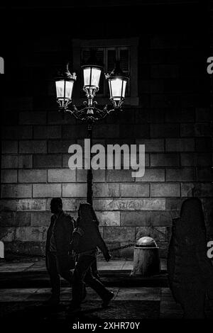 Noir et blanc grungy d'un couple tenant les mains marchant dans une rue sombre éclairée par un lampadaire Banque D'Images