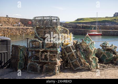 Une pile d'ustensiles de pêche : casiers à crabe, casiers à homard et filets de pêche empilés les uns sur les autres sur le quai du port de Crail Banque D'Images