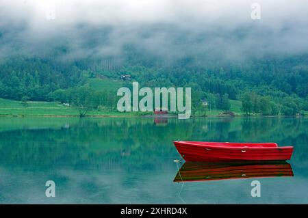 Un petit bateau rouge sur un lac calme, idylle, entouré de brouillard et de nature verdoyante, Stryn, Mindesundet, Fjordland, Norvège Banque D'Images