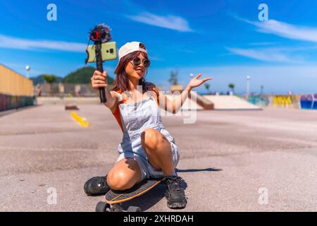 Jeune femme chinoise vlogger enregistrant une vidéo en ligne avec un téléphone portable tout en patinant dans un parc urbain Banque D'Images