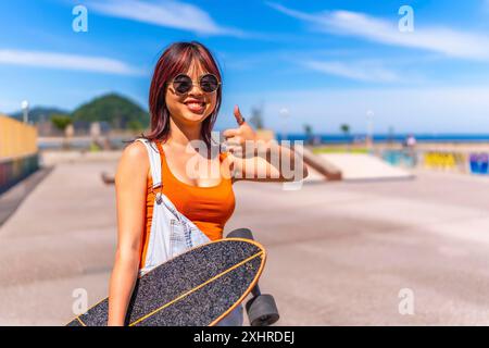 Jeune femme chinoise urbaine faisant signe de confiance avec le pouce vers le haut dans le parc de skateboard Banque D'Images