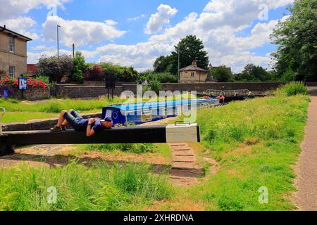 Bateau étroit traversant l'écluse sur le canal Kennett & Avon à Devizes-un homme se reposant sur le mécanisme d'écluse attendant que l'écluse se se mette en place. Prise en juillet 2024. Été. Banque D'Images