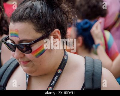 Femme avec la peinture de visage arc-en-ciel et lunettes de soleil lors d'un événement en plein air, entouré d'une foule, éditorial gay Pride cremona italie 6 juillet 2024 Banque D'Images