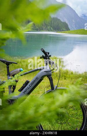 Un e-bike est garé sur le bord du lac. La nature environnante est luxuriante et verdoyante, et les montagnes peuvent être vues en arrière-plan : Stilluptal Banque D'Images