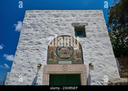 Un bâtiment blanc avec une porte verte et une mosaïque ornée sur un mur de pierre sous un ciel clair, symboles évangélistes, lion, taureau, aigle, agneau, Monastère tis Banque D'Images