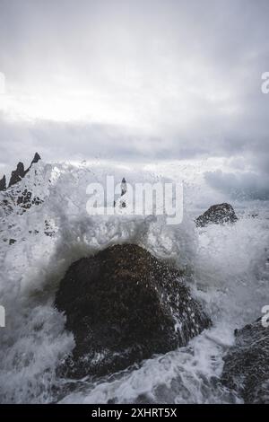 Vue de l'intérieur d'une grotte à la plage de sable noir de Reynisfjara en Islande. Montrant des vagues frappant une énorme formation rocheuse par une journée nuageuse et venteuse. Banque D'Images