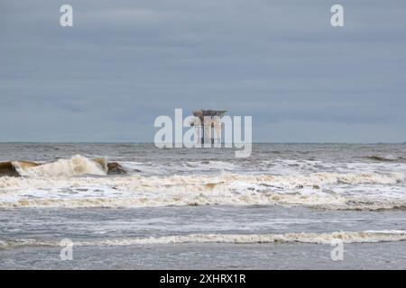 Plate-forme de production offshore près de l'île néerlandaise Ameland, surfe près de la plage au premier plan Banque D'Images