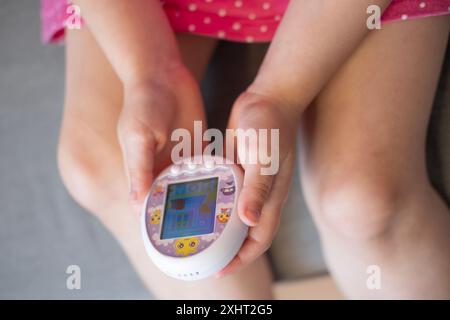 La main de l'enfant berce doucement le jouet Tamagotchi, évoquant la nostalgie de l'engouement populaire des animaux de compagnie virtuels des années 1990, développant l'empathie, nourrissant les souvenirs d'enfance, Fran Banque D'Images