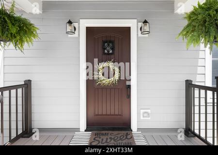 Un détail de porte d'entrée en bois avec revêtement en vinyle gris, plancher de terrasse composite et pluie, et des lumières montées à côté de la porte. Banque D'Images