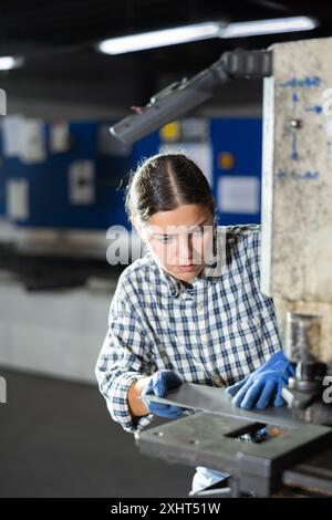 Jeune femme coupant des trous dans le métal sur la machine Banque D'Images