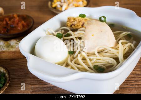 Plat péruvien typique connu sous le nom de soupe au poulet, dans un bol en bois avec citron et ciboulette. bien Banque D'Images